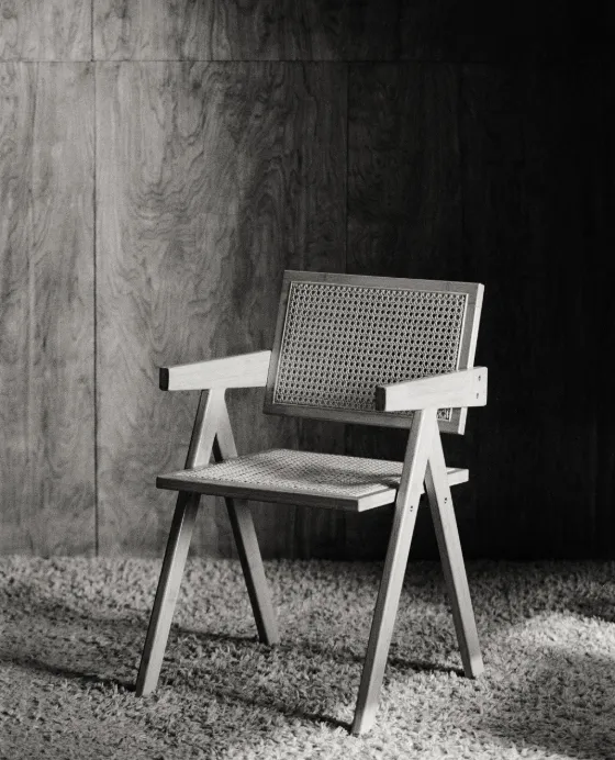 An empty cane-and-wood armchair on a shag rug, waiting for someone to sit down